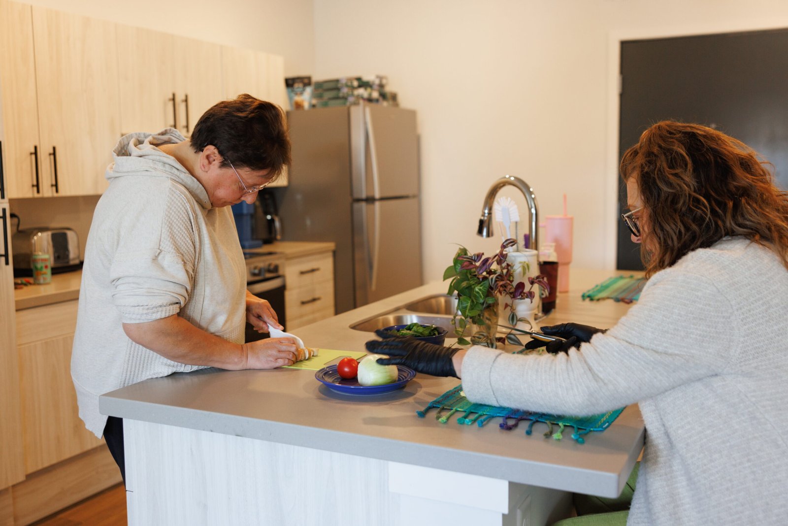 Two women prepare vegetables together at a kitchen island.