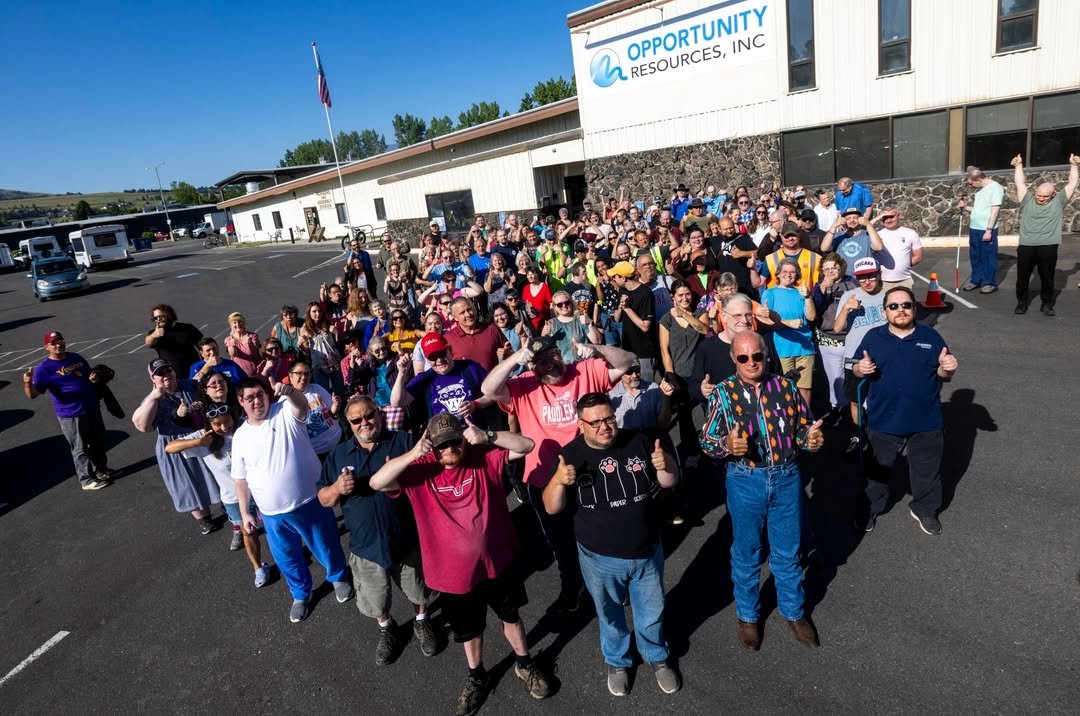 A large crowd of ORI clients and staff give a thumbs-up in the parking lot in front of the Opportunity Resources, Inc. building.