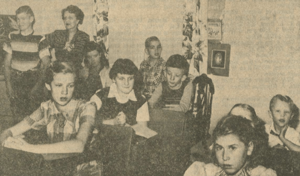 A newspaper photo of Opportunity School students seated at desks in a classroom, with a teacher standing at the back.