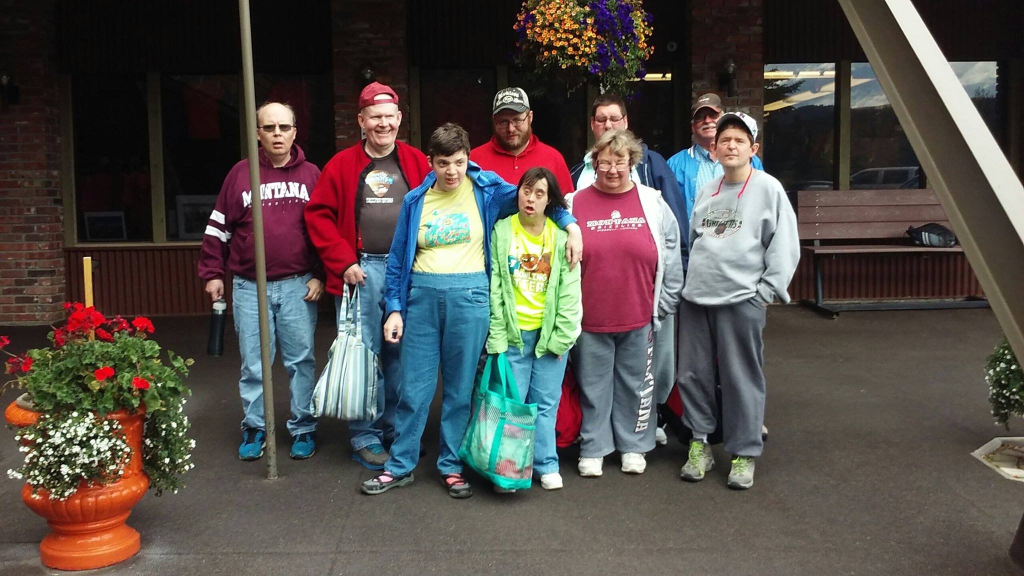 A group of ORI clients and staff stand together outside a brick building beside hanging flower baskets.